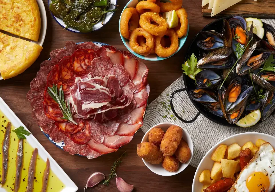 Mesa con platos tradicionales de comida española como tortilla, embutidos, mariscos y tapas variadas