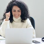 Mujer latinoamericana celebrando frente al portátil tras solicitar el arraigo social en España